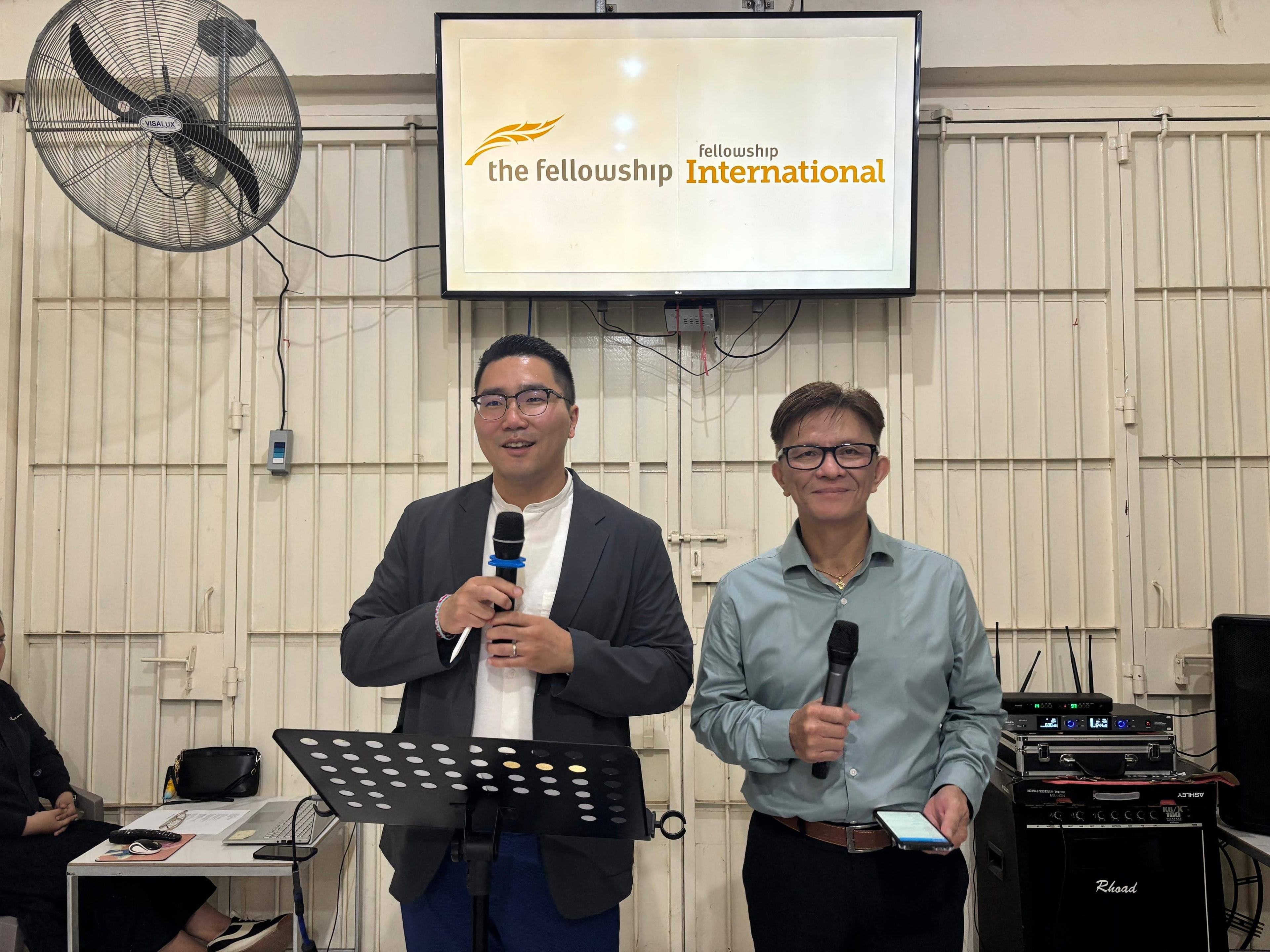 Byron Chae and Edwin Karwur speaking at a local church service in Indonesia beneath the Fellowship International banner
