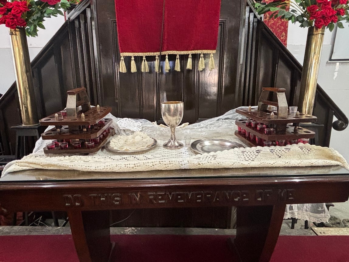 The Lord's Supper table at Carey Baptist Church inscribed with 'Do This in Remembrance of Me', set with communion cup, bread, and trays